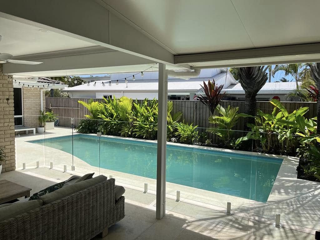 Frameless glass pool fence with white spigots viewed from a covered alfresco area